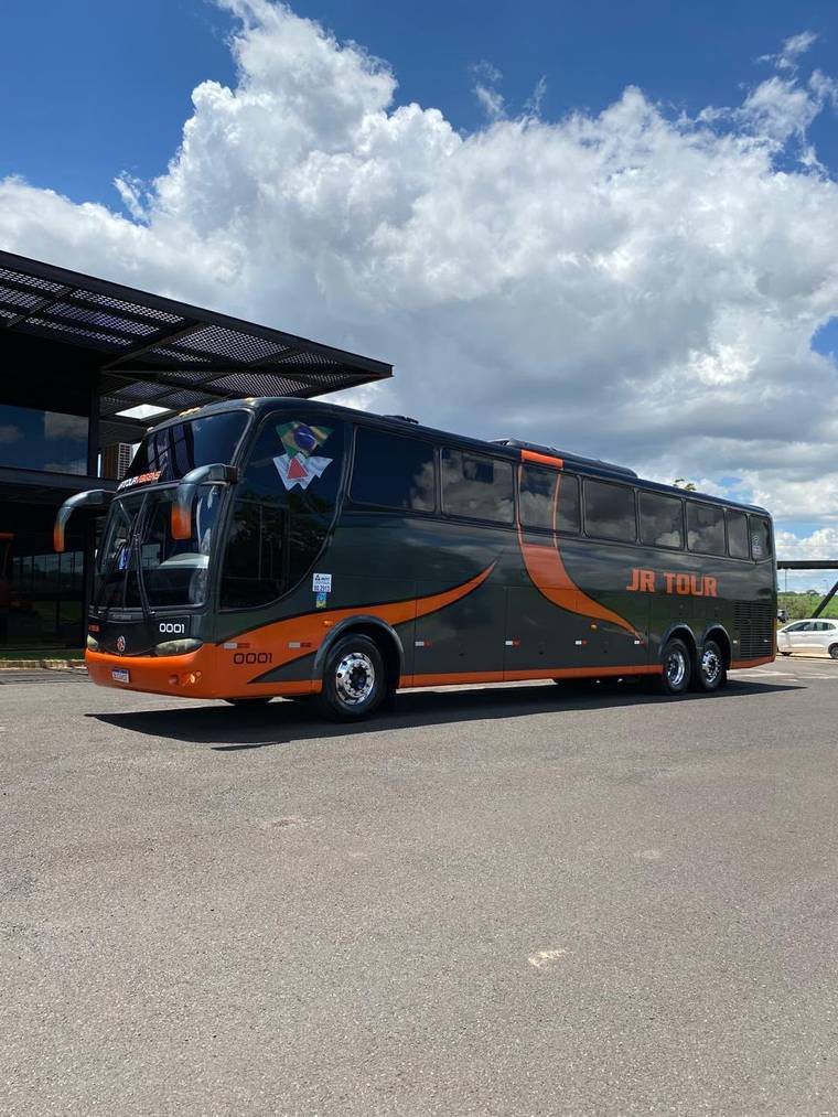 Ônibus rodoviário da JR TOUR na cor escura com grafismo laranja, estacionado.